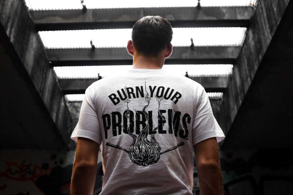 Man standing indoors, wearing a t-shirt with 'Burn Your Problems' text, viewed from behind.